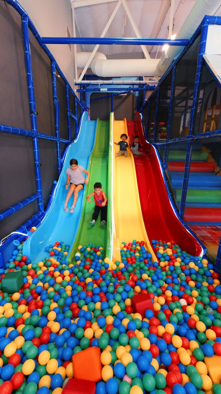 Two kids coming down the rainbow slides into the ball pit