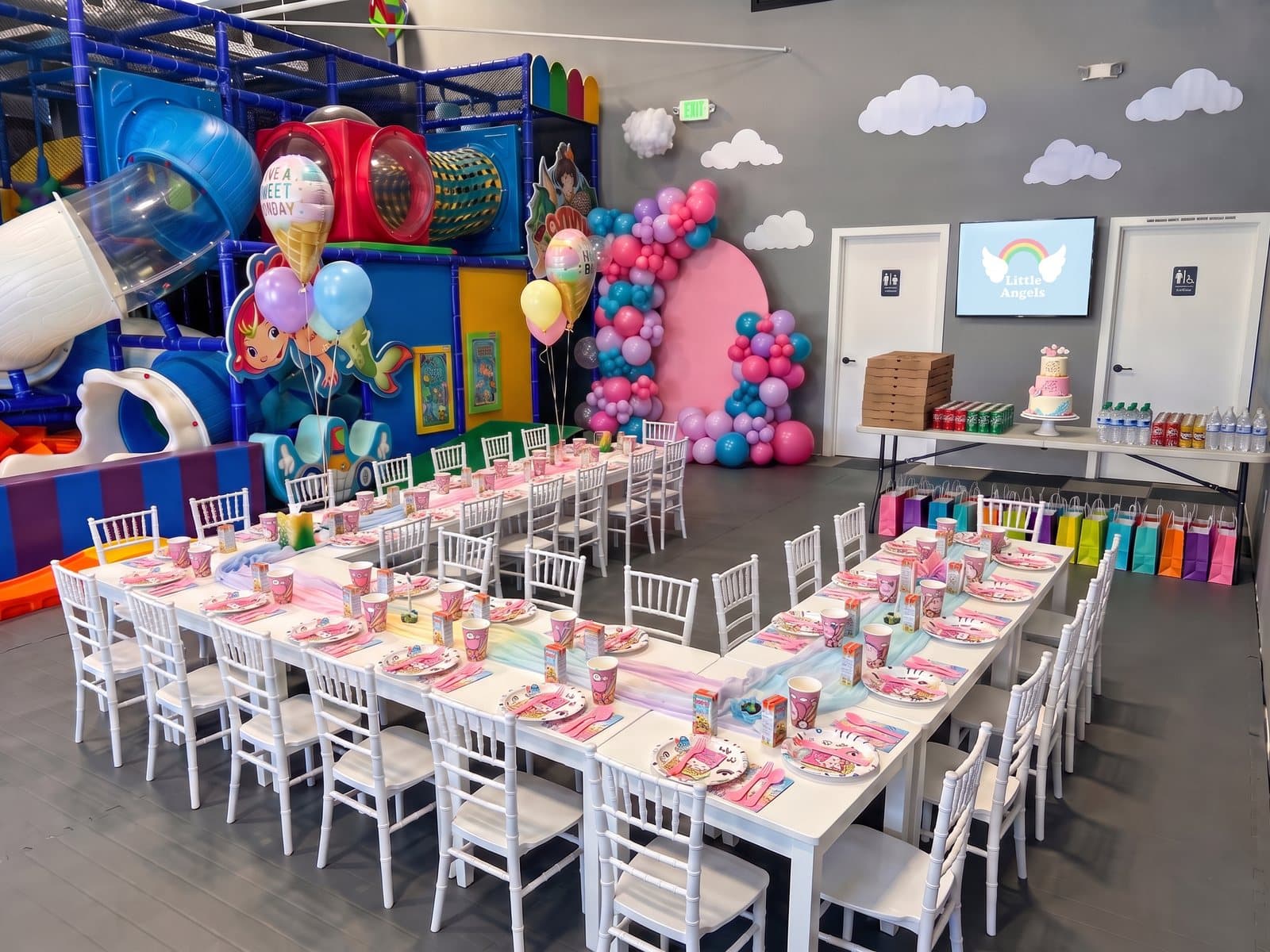 Two long party tables for thirty with a balloon arch backdrop, a tiered cake, pizzas and drinks in the party room