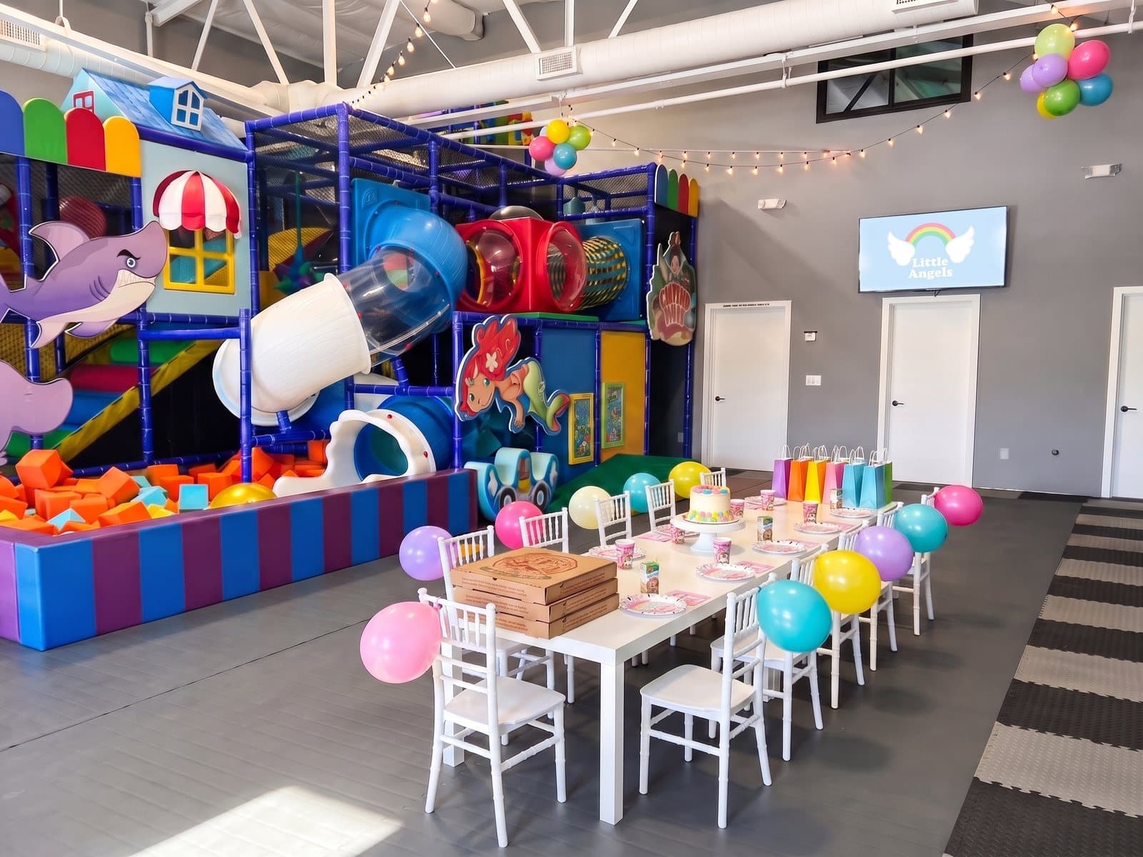 A small party table for ten in the party room, with a cake stand, juice boxes, pizza and goodie bags