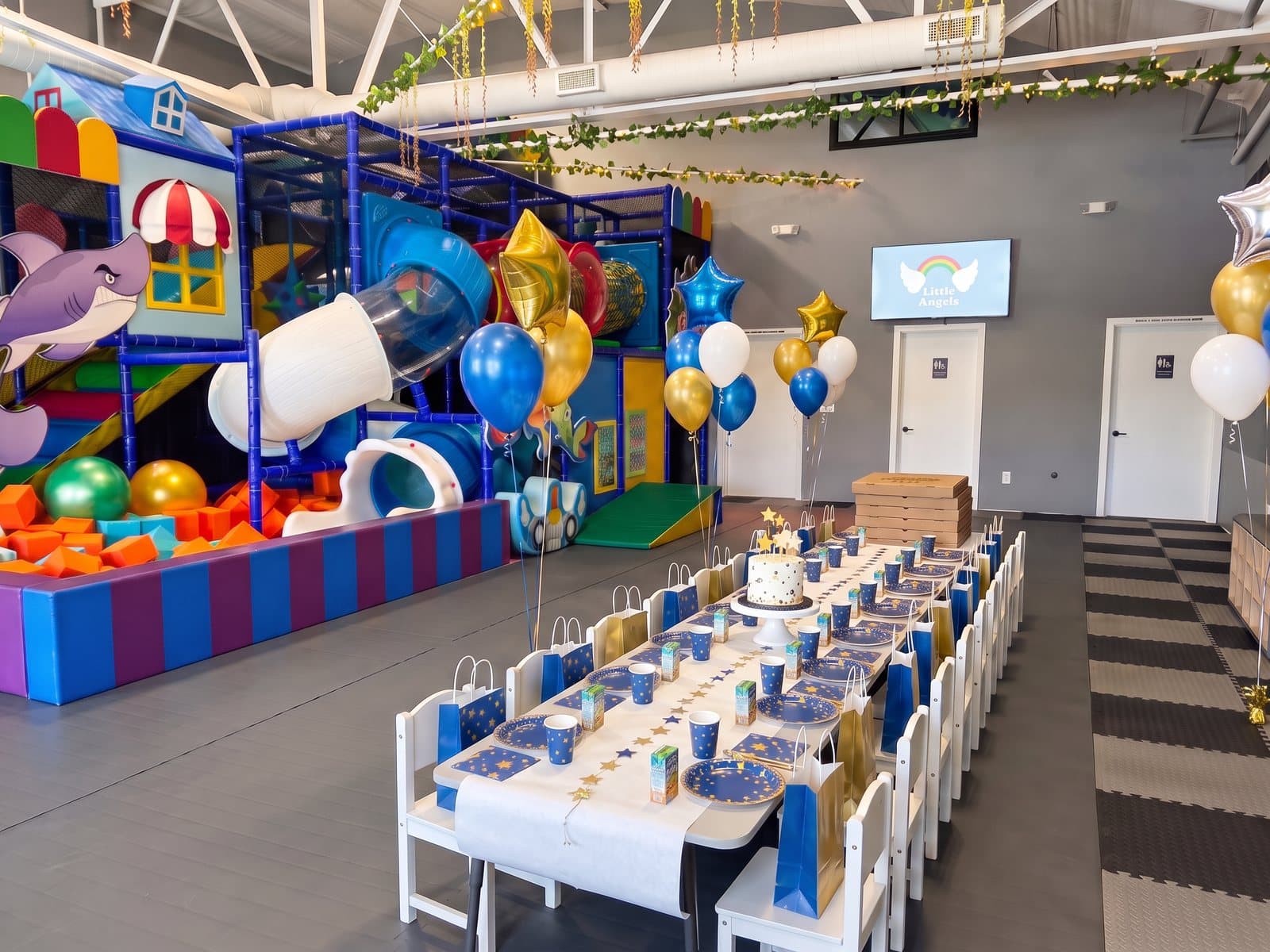 A long star-themed party table for twenty in the party room, with a cake stand, pizzas and balloons