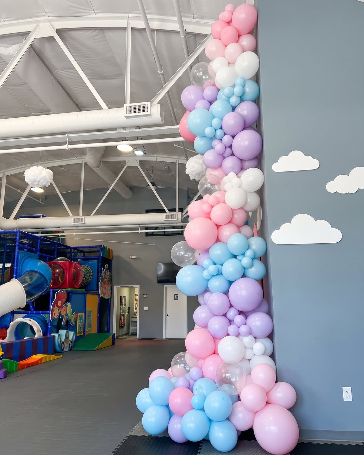 A pastel balloon garland on the party room wall next to the cloud cut-outs
