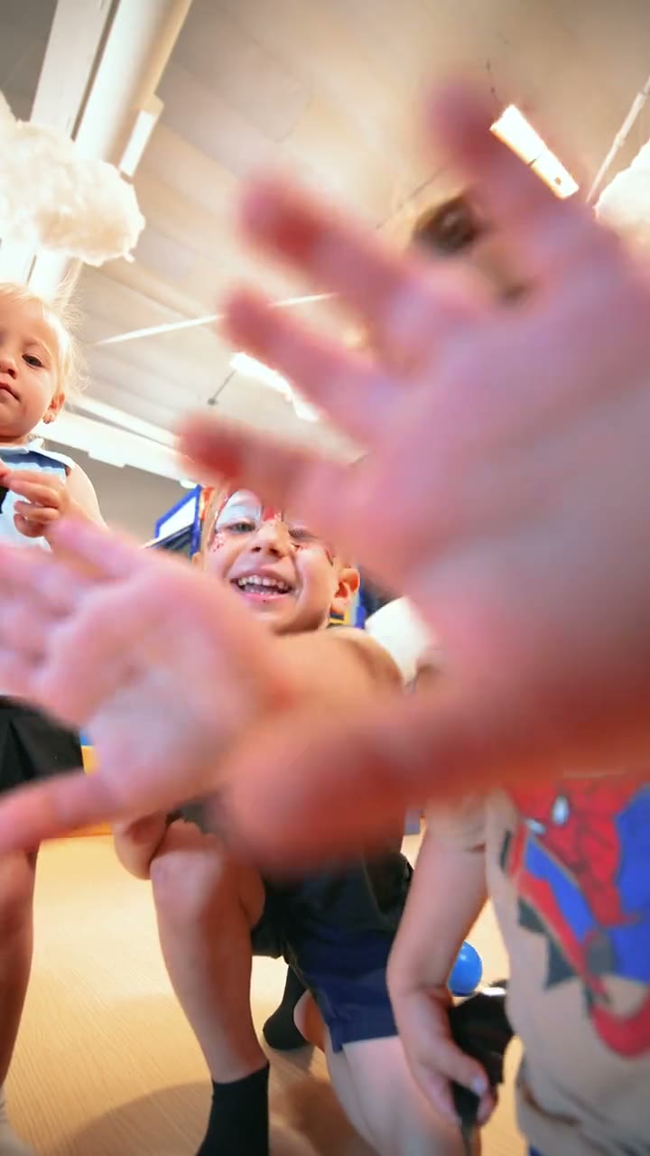 Kids waving at the camera on the play floor under the hanging clouds